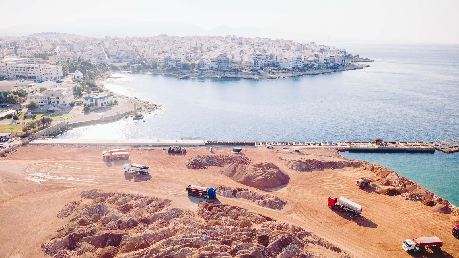 Reinforced concrete caisson construction during port expansion works at the Port of Piraeus with heavy trucks transporting aggregate materials.By Nafpliotis Bros